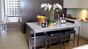 Una cocina moderna con una isla central, taburetes de bar, un frutero y orquídeas blancas.
