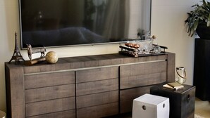 Una sala de estar moderna con un televisor de pantalla plana grande montado en un mueble de madera, una pequeña mesa de centro y elementos decorativos, incluyendo un globo y una escultura de vidrio.
