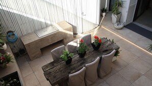 Una mesa de madera para comer con seis sillas, rodeada de plantas en macetas y un pequeño banco.