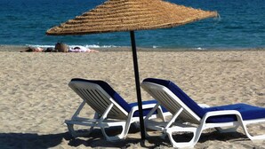 Two white lounge chairs with blue cushions and a woven beach umbrella on a sandy beach with the ocean in the background. - Spacious T2 cabin, terrace, pet-friendly (Sète)