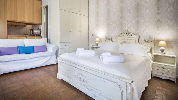 A bedroom with a large bed, a sofa, a wardrobe, and a nightstand with a lamp.