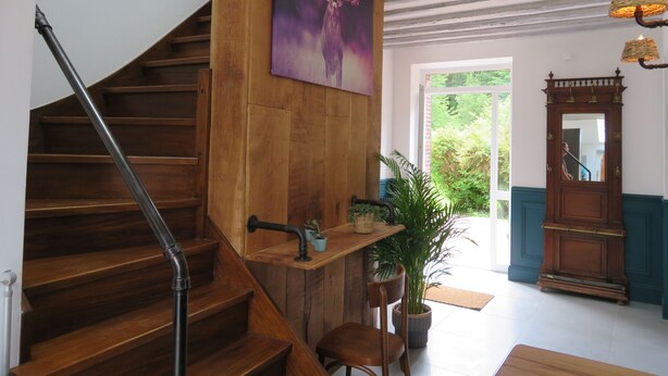 A wooden staircase with a handrail, a wall-mounted painting of a deer, a potted plant, a wooden chair, and a mirror with a decorative frame.