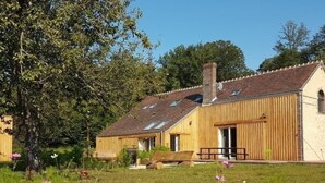 A rustic wooden house with a sloped roof and a chimney, surrounded by a grassy field with wildflowers.