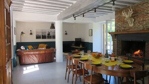 A dining area with a brick fireplace, a round wooden table set for four, and a sofa in the background.