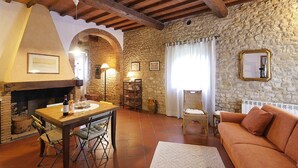 Una sala de estar acogedora con una pared de piedra, una chimenea, una mesa de madera con sillas, un sofá y una lámpara.