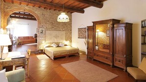 Un dormitorio acogedor con un arco de piedra, una cama de madera, una mesita de noche, un armario de madera y una araña.