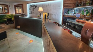 Un área de bar con mostrador de madera, un sofá tapizado en verde y una pared con un cuadro grande.