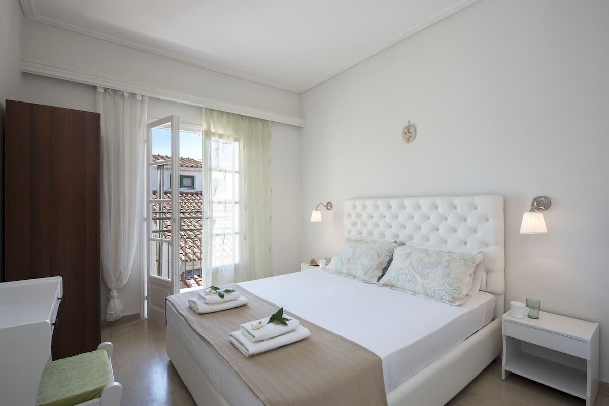 A hotel room with a large bed, a wooden chair, a nightstand, and a window with curtains.