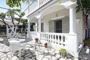 A white building with a balcony, stone flooring, and outdoor furniture. - The Orange Garden (Corfu)