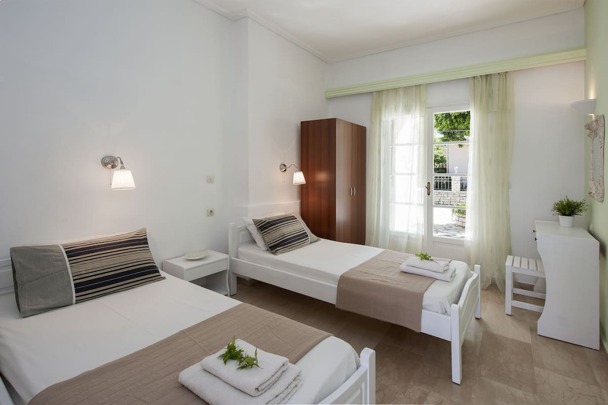 A hotel room with two single beds, a wardrobe, a small table, and a window with curtains.