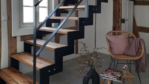 A staircase with wooden steps and black metal railings, a wicker chair with a cushion, and a small table with books and a vase of flowers. - Modern vacation apartment "Tante Emma"  (Sinsheim)