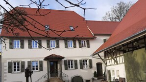 A traditional building with a red-tiled roof, multiple windows with shutters, and a cobblestone courtyard. - Modern vacation apartment "Tante Emma"  (Sinsheim)
