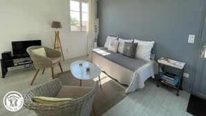 Een slaapkamer met een bed, twee stoelen, een klein tafeltje, een televisie en een boekenkast.