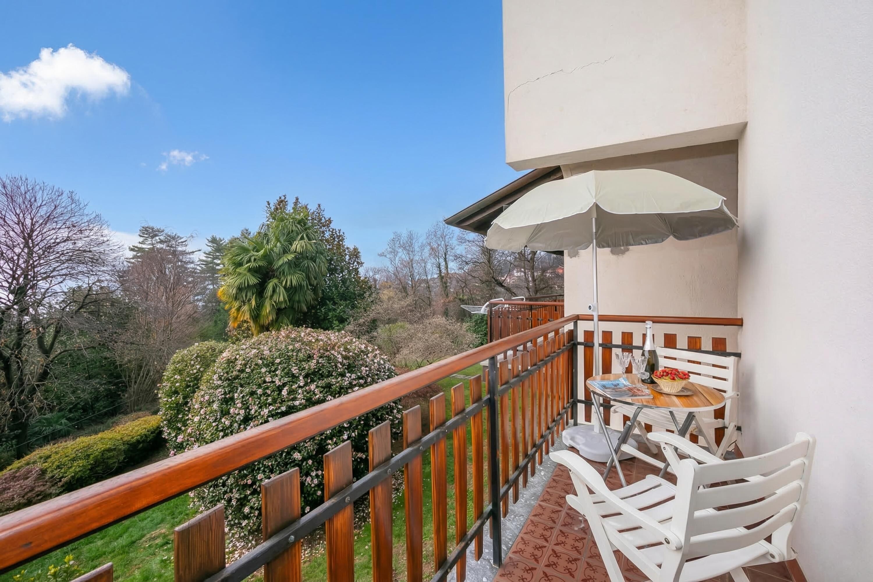 A balcony with a wooden railing, a table with chairs, and an umbrella.