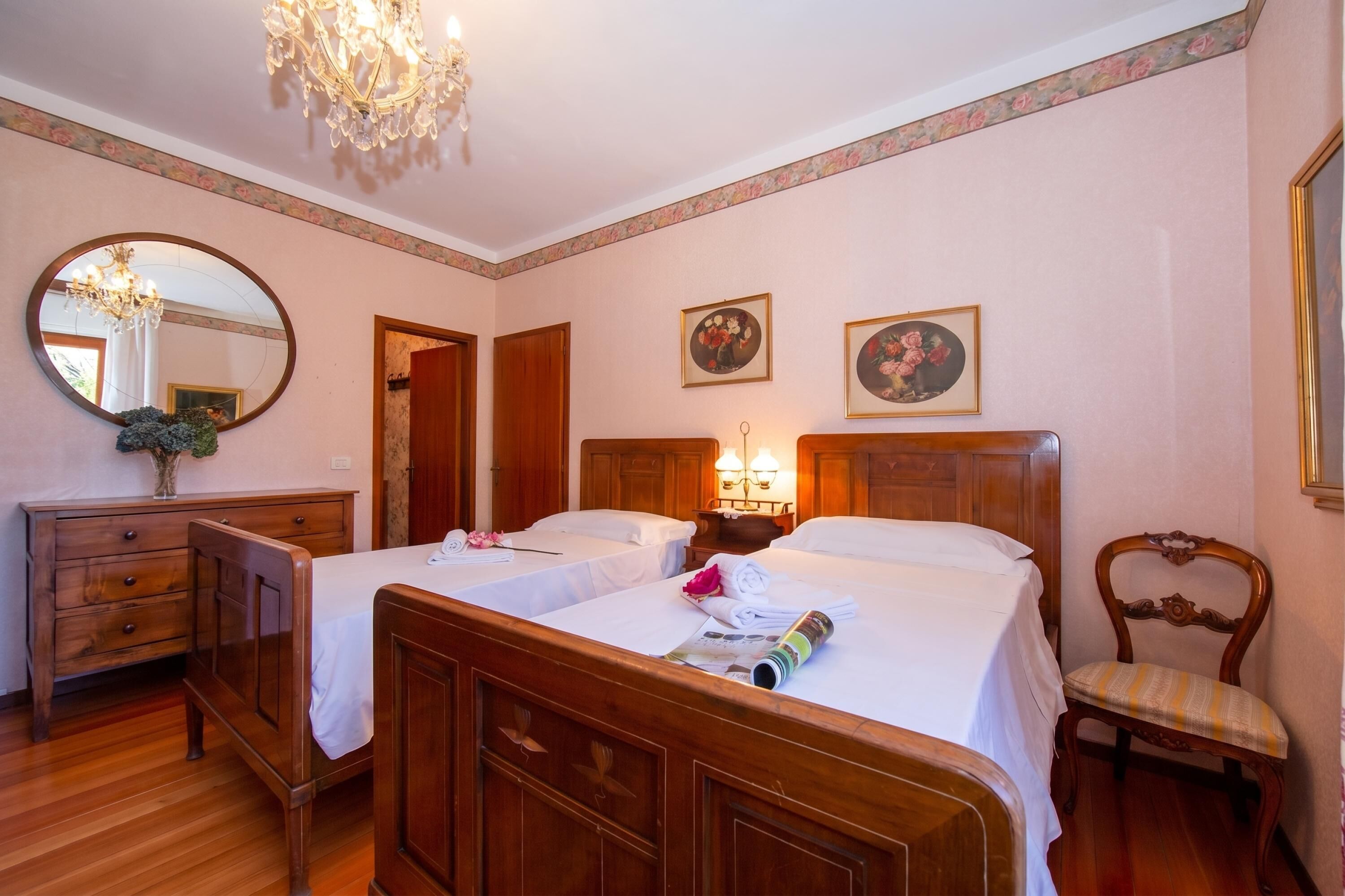 A hotel room with two wooden beds, a wooden dresser, a chair, a mirror, and two wall-mounted lamps.