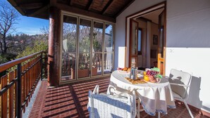 Un balcón con barandilla de madera, una mesa con mantel blanco y una silla.