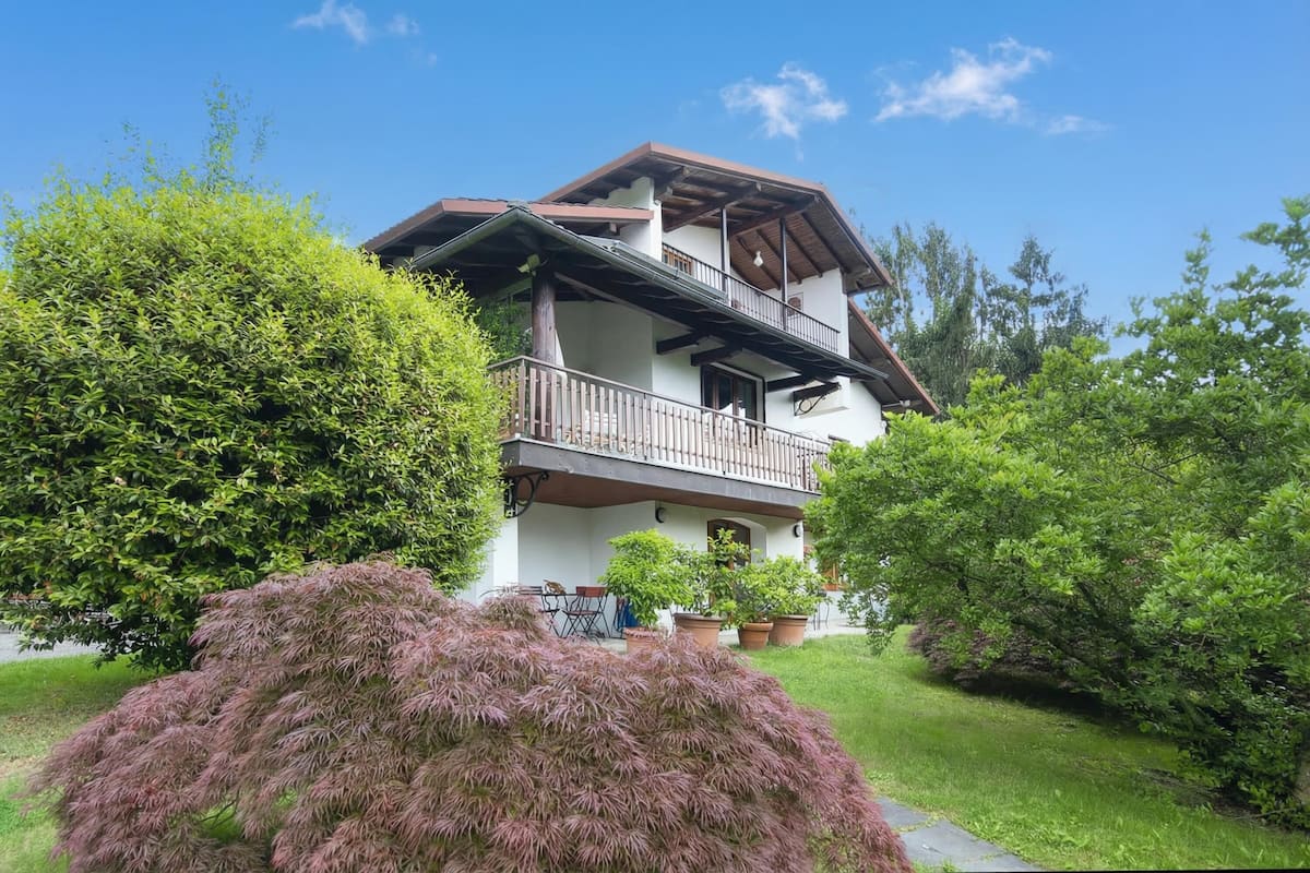 A two-story house with a balcony, surrounded by lush greenery.