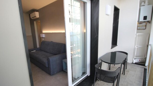 A compact living space with a sofa, a small table, and chairs, a sliding glass door leading to a balcony, and a radiator on the wall.