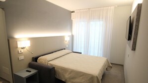 A hotel room with a bed, bedside table, and a small stool.