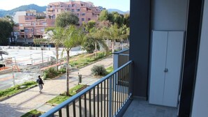 A balcony with a view of a pedestrian street, palm trees, and multi-story buildings in the background.
