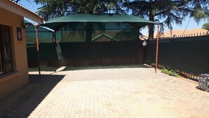 A covered outdoor area with a paved floor, a green canopy, and a fence. - C- Land Guest house Meyerton (Meyerton)
