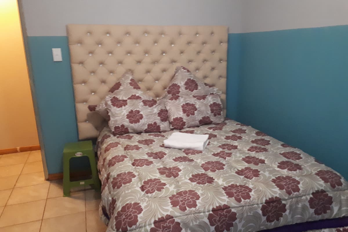 Ein Bett mit einem geblatteten Kopfteil, floralem Bettzeug und einem Nachttisch in Grün.