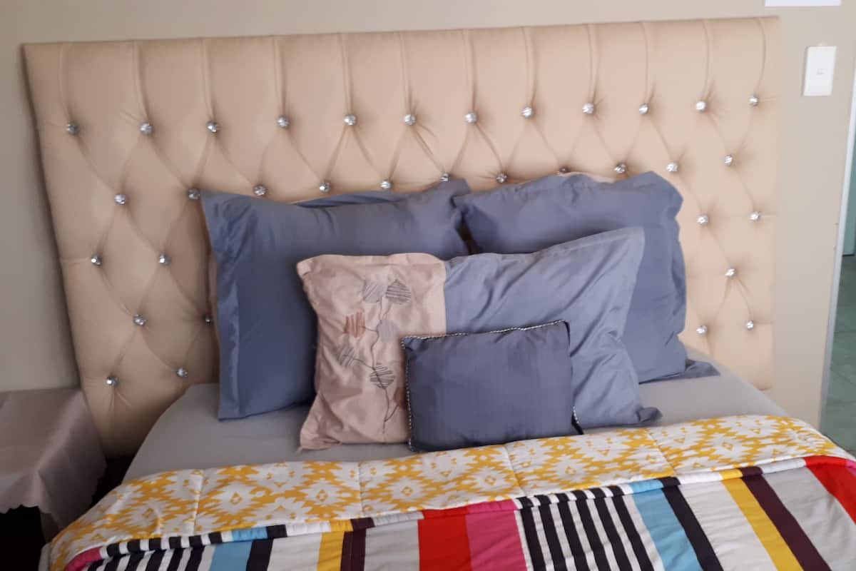 Ein Bett mit einer gesteppten Kopfteil, mehreren Kissen und einer farbenfrohen, gestreiften Bettdecke.
