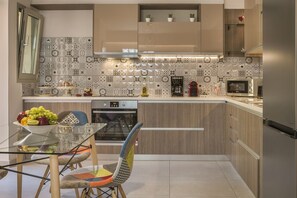 A modern kitchen with a glass dining table, colorful chairs, and a variety of appliances including a microwave and oven.