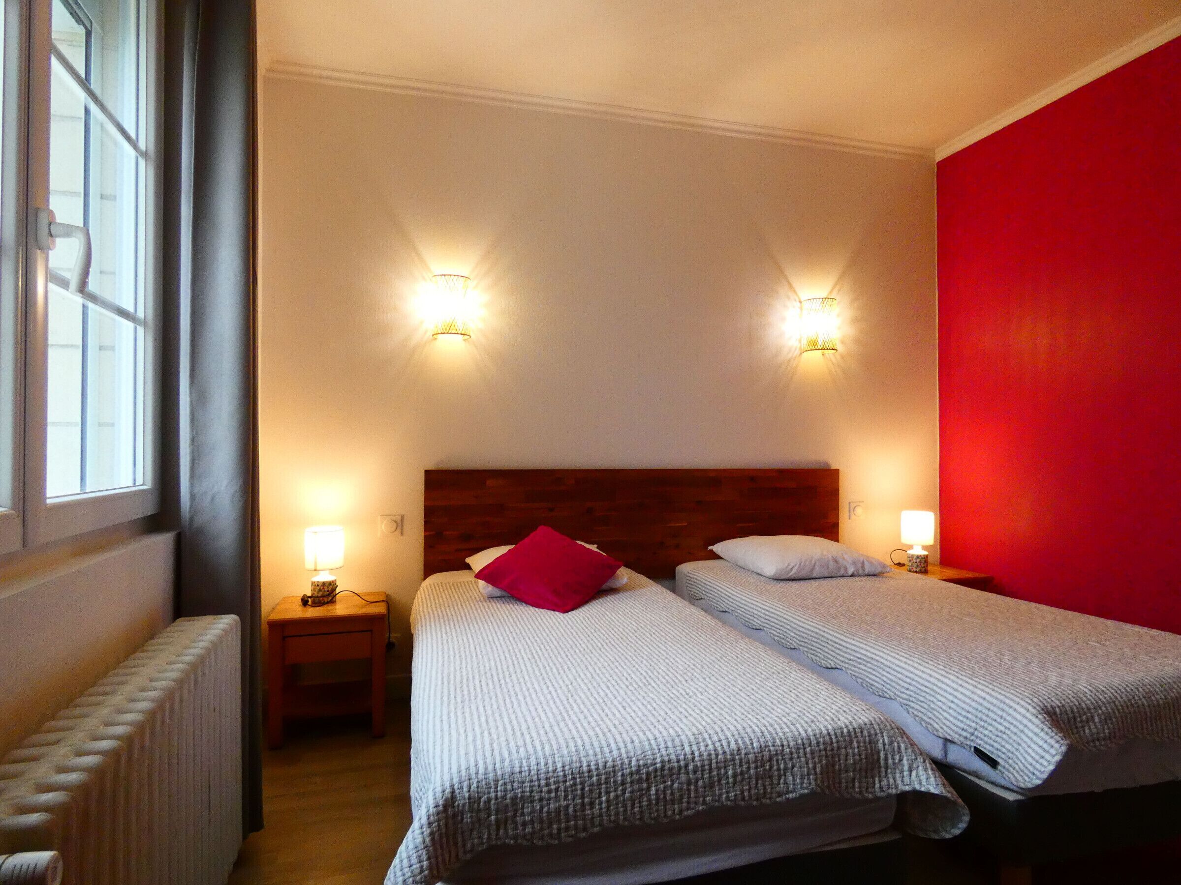 Une chambre d’hôtel avec deux lits, un mur d’accent rouge et deux lampes fixées au mur.