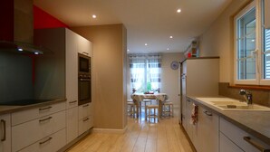 A modern kitchen with built-in appliances, a dining area with a table and chairs, and a window with blinds. - Charming Stone House in Calm Senonches - Modern Amenities & Large Garden (Senonches)