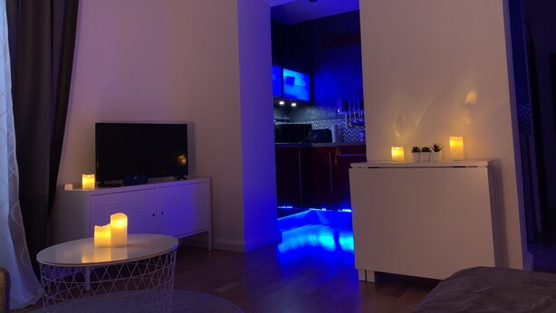 A modern living room with a flat-screen TV, a round table with candles, and a small white cabinet. - Comfort and calm in the heart of Annecy (30m2 hyper center) (Annecy)