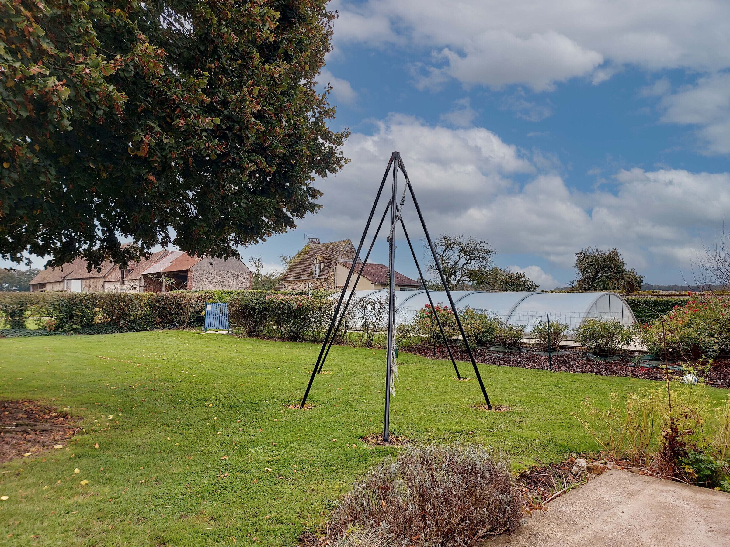 Ein Garten mit Schaukel, Gewächshaus und Steingebäuden im Hintergrund.