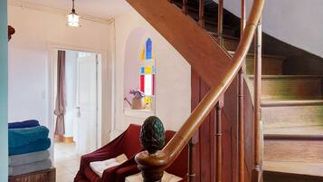 A staircase with wooden handrails and a red cushioned bench in a room with a white door, a window with colorful stained glass, and a ceiling light fixture.