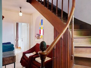 A staircase with wooden handrails and a red cushioned bench in a room with a white door, a window with colorful stained glass, and a ceiling light fixture. - Charming Farmhouse with Private Pool & Garden near Paris (La Chapelle-Fortin)