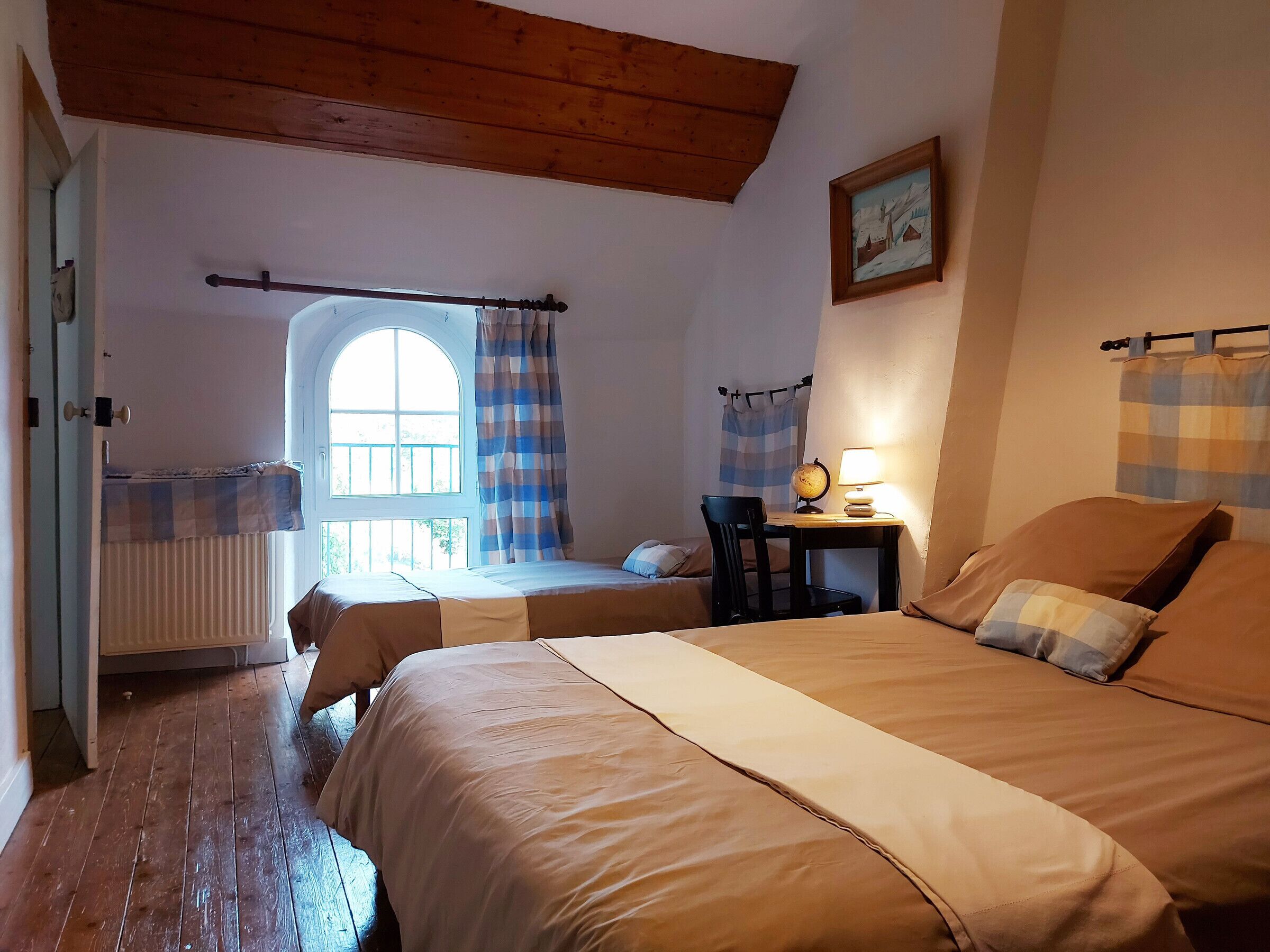 Ein gemütliches Schlafzimmer mit zwei Betten, einer Holzbalkendecke, einem Globus auf einem Nachttisch und einem Fenster mit Vorhängen.