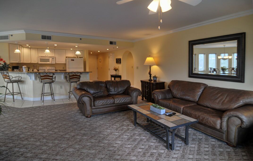 A living room with two brown leather sofas, a coffee table, and a kitchen in the background.