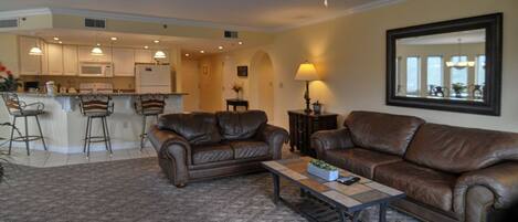 A living room with two brown leather sofas, a coffee table, and a kitchen in the background.