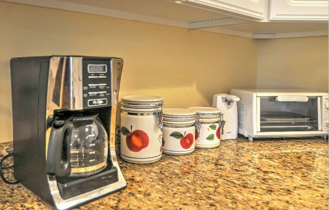 Una cocina con cafetera, tostadora y tres tarros decorados con motivos frutales.