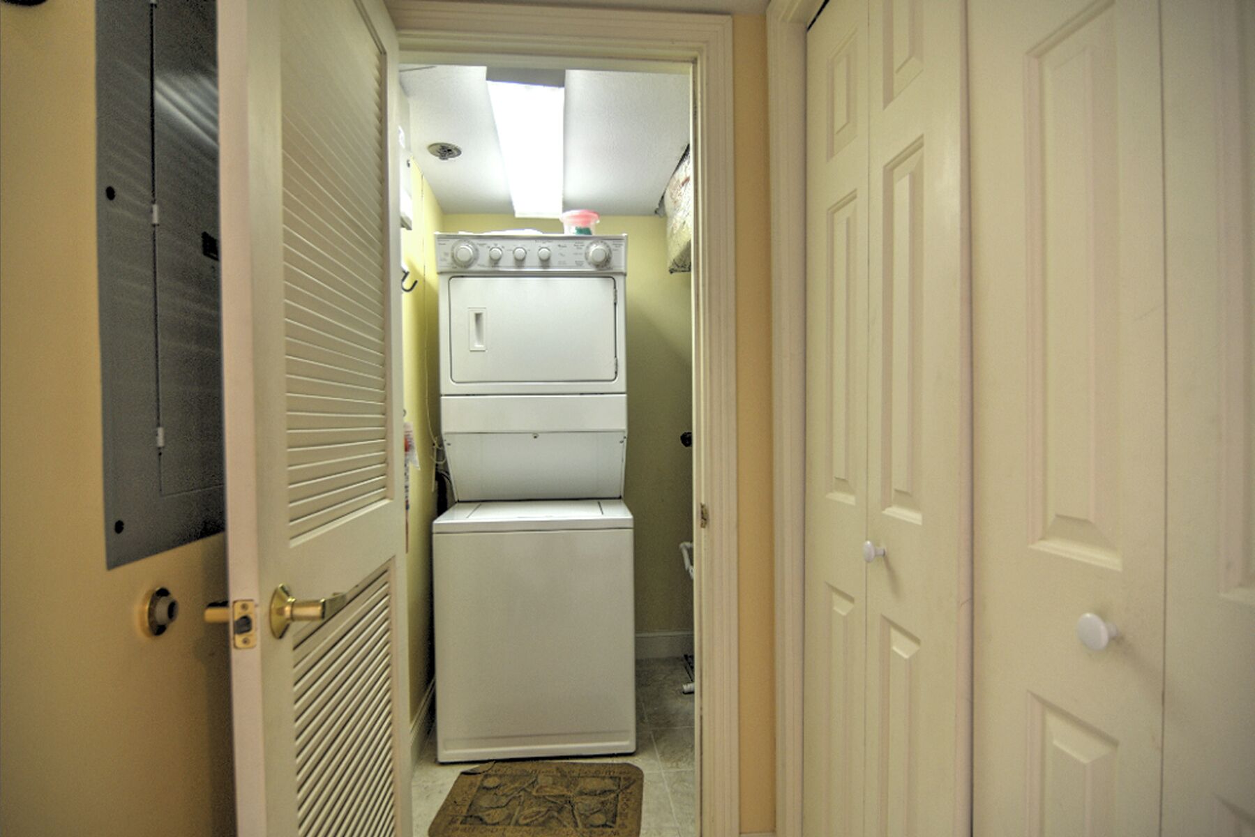 A laundry room with stacked washers and dryers, a vented dryer, and a door leading to another room.