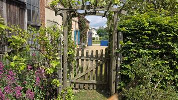 A wooden gate leading to a garden with a pergola, surrounded by various plants and a fence.