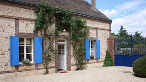 Een huis met een grindpad, een blauwe poort en een bakstenen schoorsteen.