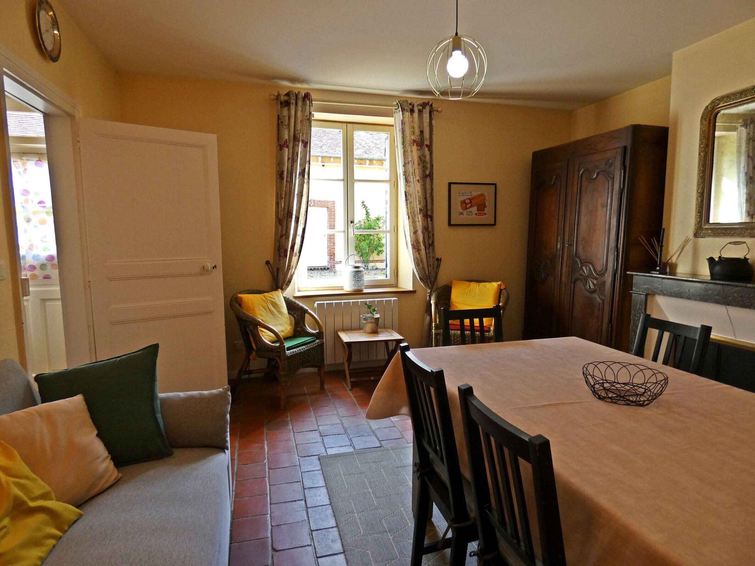A dining area with a table, chairs, a sofa, a window with curtains, a radiator, and a wall-mounted clock.