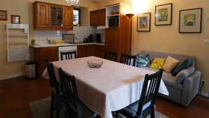 A dining area with a table, chairs, a kitchen with wooden cabinets, a microwave, and a water heater. - Charming Cottage with Pool Near Dreux and Chartres - Sleeps 4 (Le Boullay-Thierry)