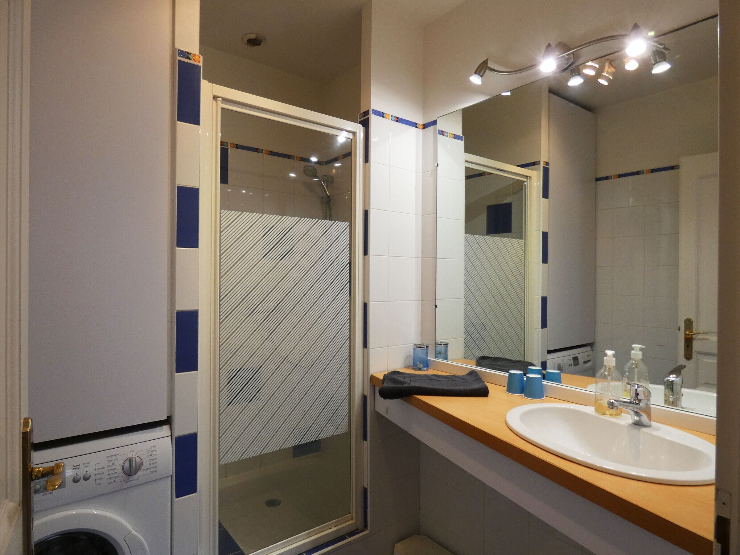 Une salle de bain avec une douche à parois de verre, un lavabo avec un miroir et un lave-linge.
