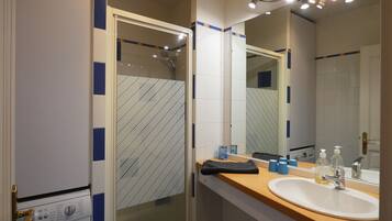 Une salle de bain avec une douche à parois de verre, un lavabo avec un miroir et un lave-linge.