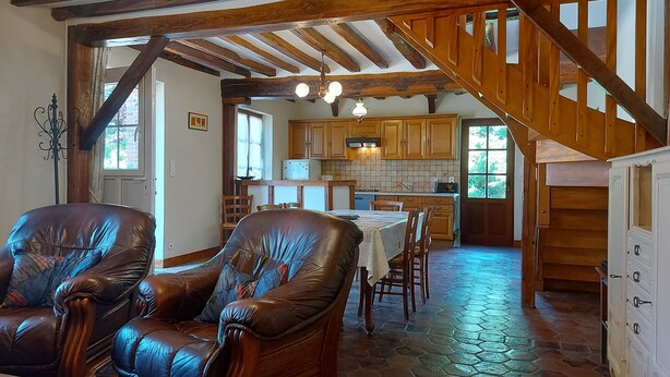 Un intérieur rustique avec des fauteuils en cuir, une table à manger, des poutres en bois et un coin cuisine.