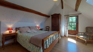 Une chambre avec un lit en bois, une table de chevet avec une lampe, une armoire en bois, une fenêtre avec des rideaux et une chaise.