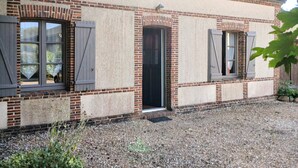 Un bâtiment à deux étages avec une façade en briques, une allée en gravier et une porte donnant sur l’entrée.
