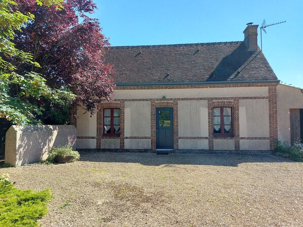 A building with a brick facade, a tiled roof, and a gravel driveway. - Charming Renovated Cottage with Garden, BBQ, WiFi & Family Amenities Near Paris (La Saucelle)