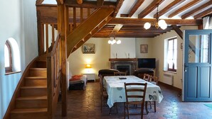 Un intérieur rustique avec un escalier en bois, un coin repas avec une table dressée pour quatre personnes et une cheminée.